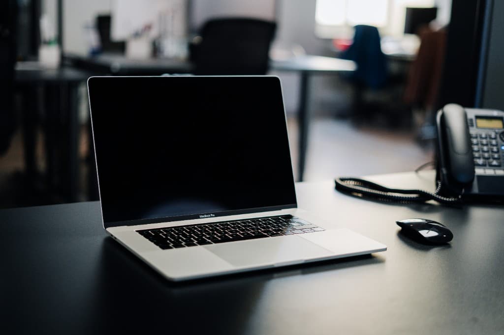 Laptop and desk phone on an office desk — ready to take your call or brief